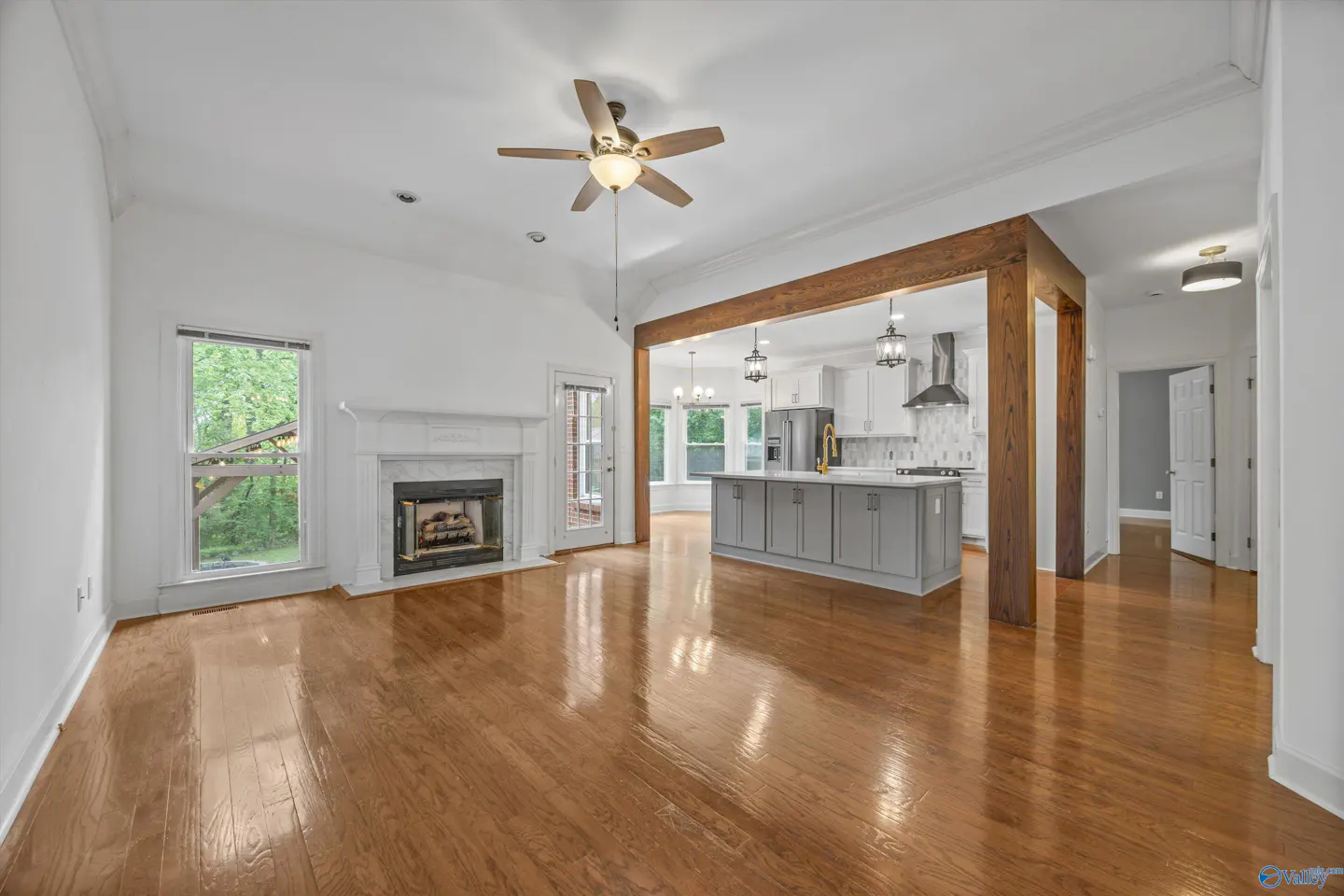 Open-concept living space with hardwood floors, white walls, fireplace, and kitchen island with gray cabinets.