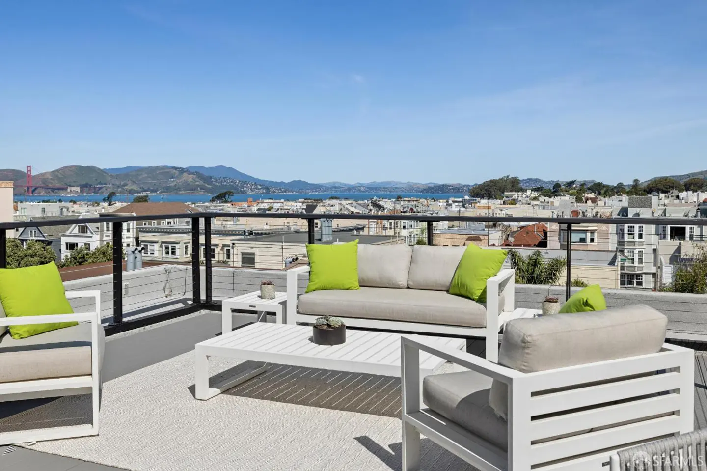 Rooftop patio with white furniture, green pillows, and a view of San Francisco and the Golden Gate Bridge.