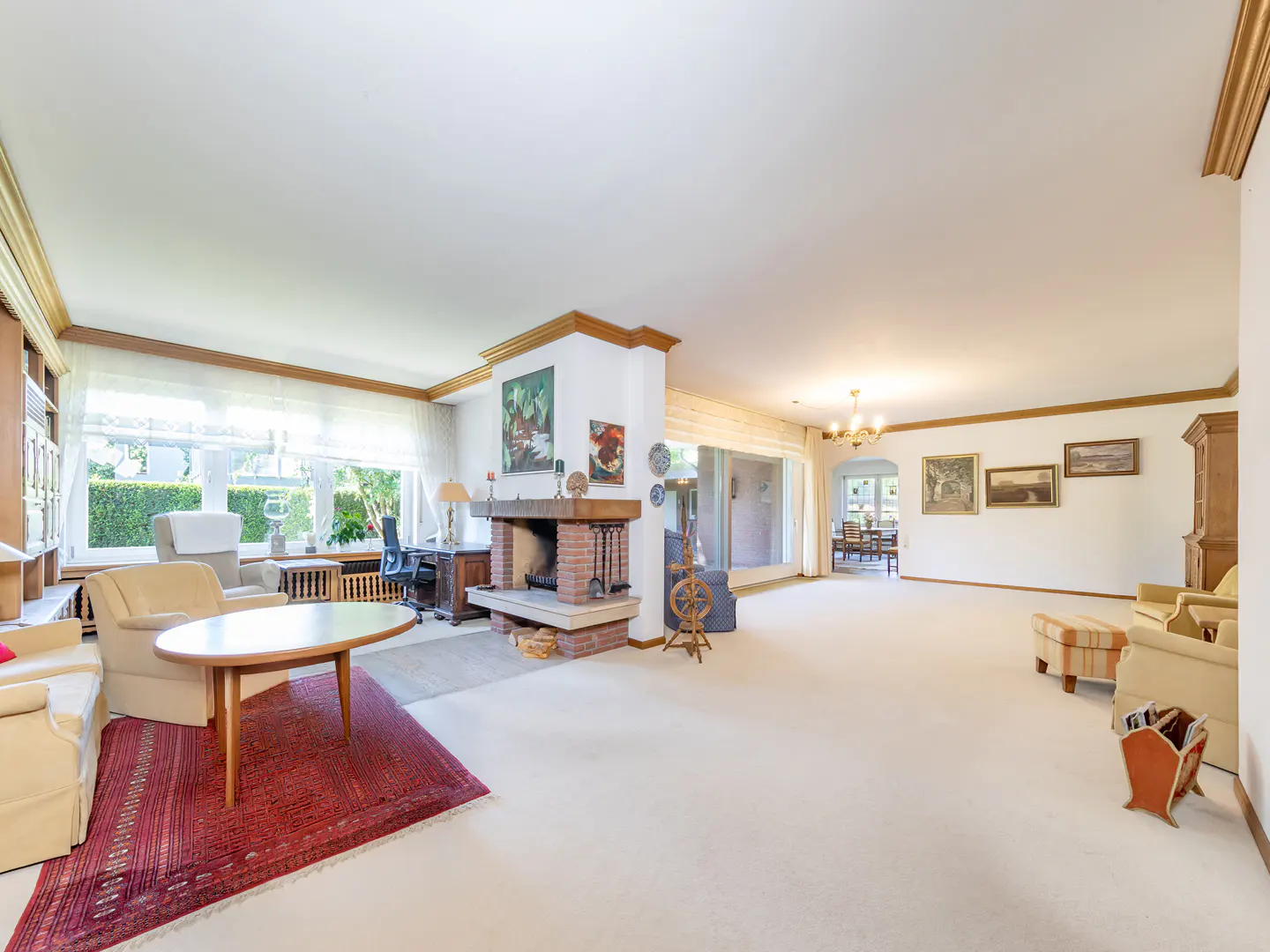 Spacious living room with a brick fireplace, beige carpet, red area rug, and seating areas leading to a dining room.
