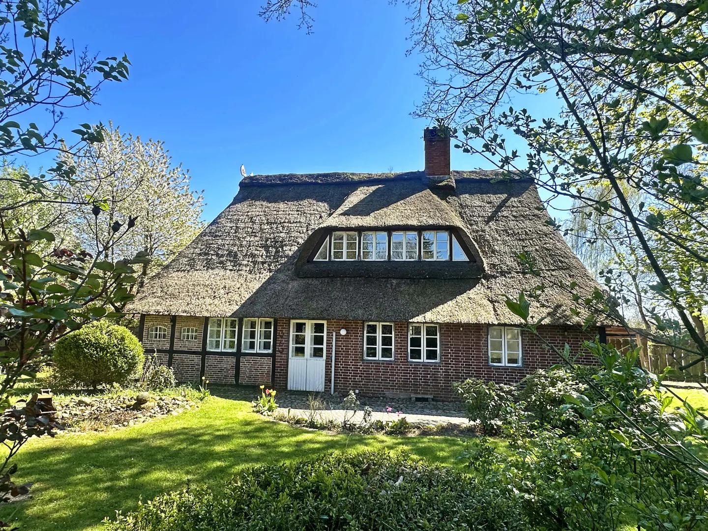 Exterior view of a brick house with a thatched roof and white trim on a sunny day.