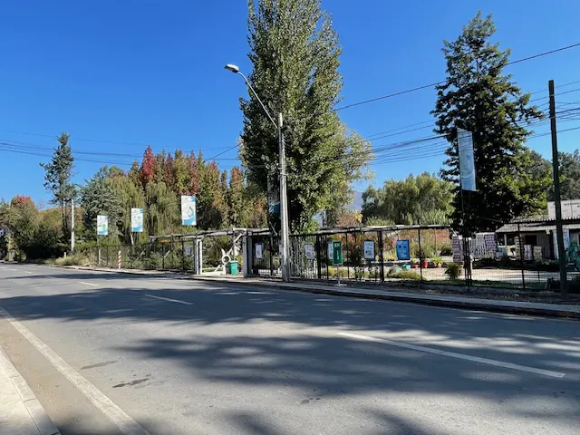 Street view of a park with trees, a fence, and posters under a clear blue sky.