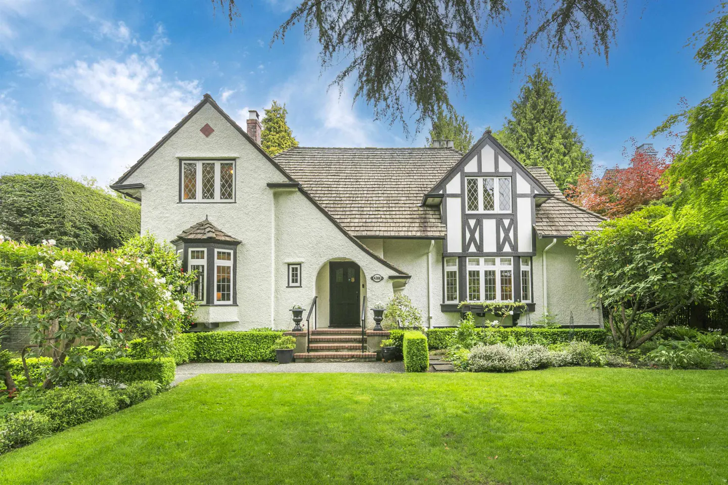 Two-story Tudor-style house with white stucco, black trim, and a green lawn.