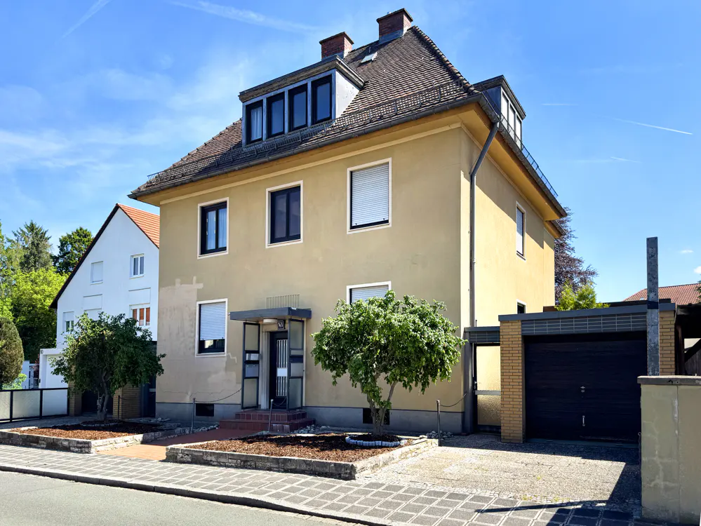 Two-story beige house with a brown roof, black window frames, and a garage on a sunny day.