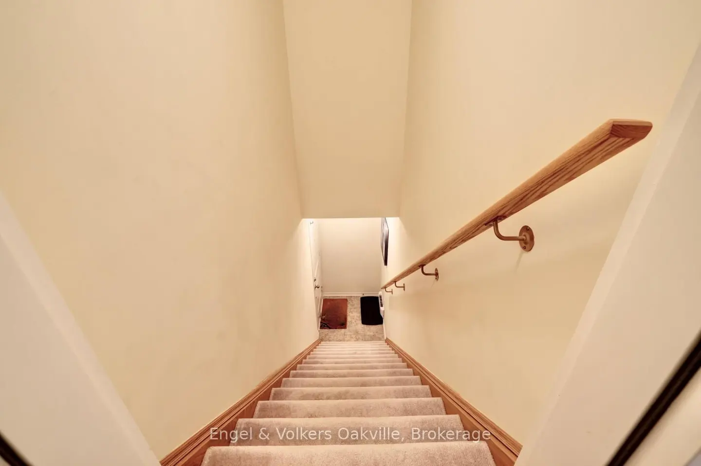 Beige carpeted stairs lead down with a wooden handrail on the right wall in a home interior.