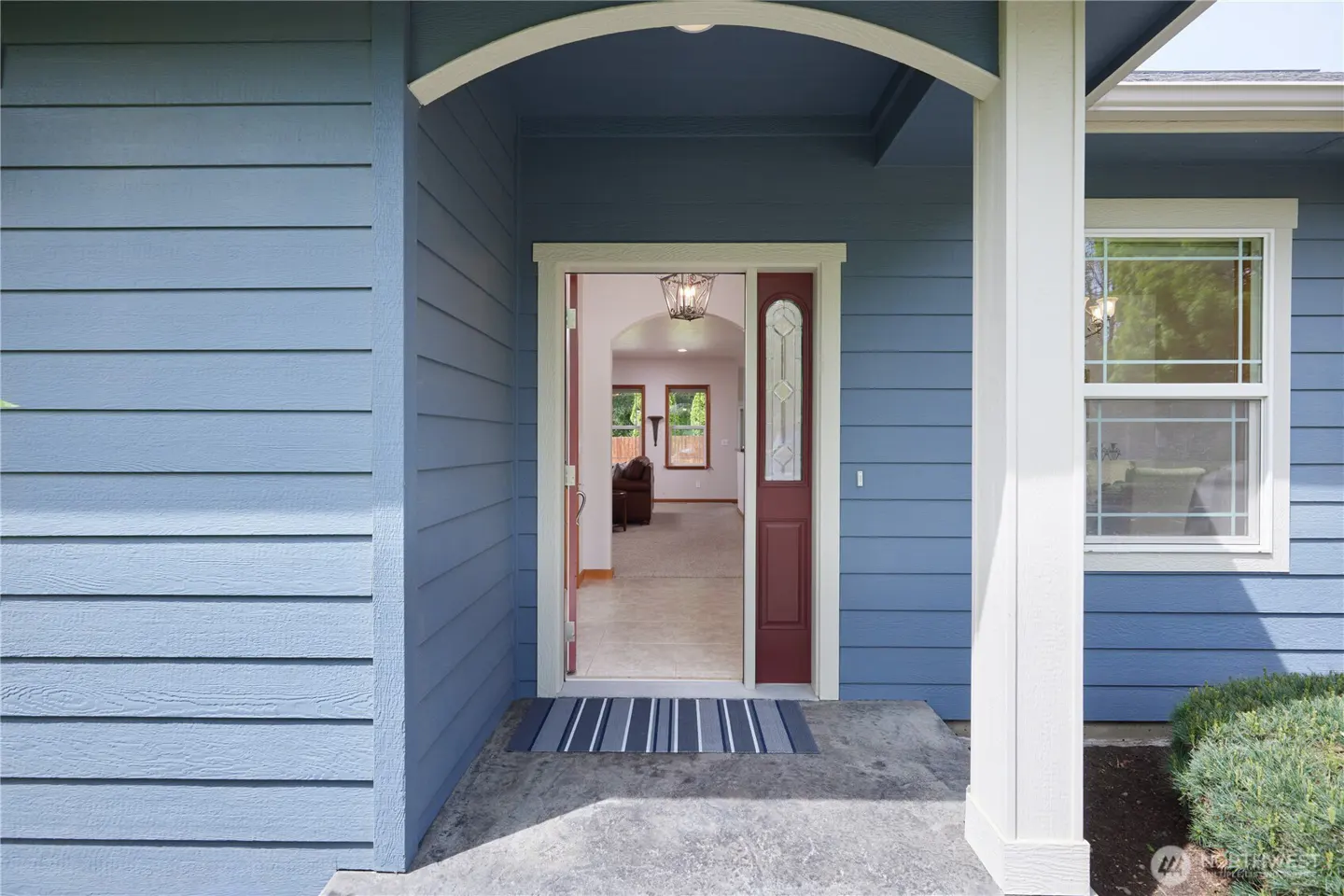 Exterior view of a blue house with an open front door. A striped doormat sits on the concrete porch. Interior view of a living room with brown leather furniture.
