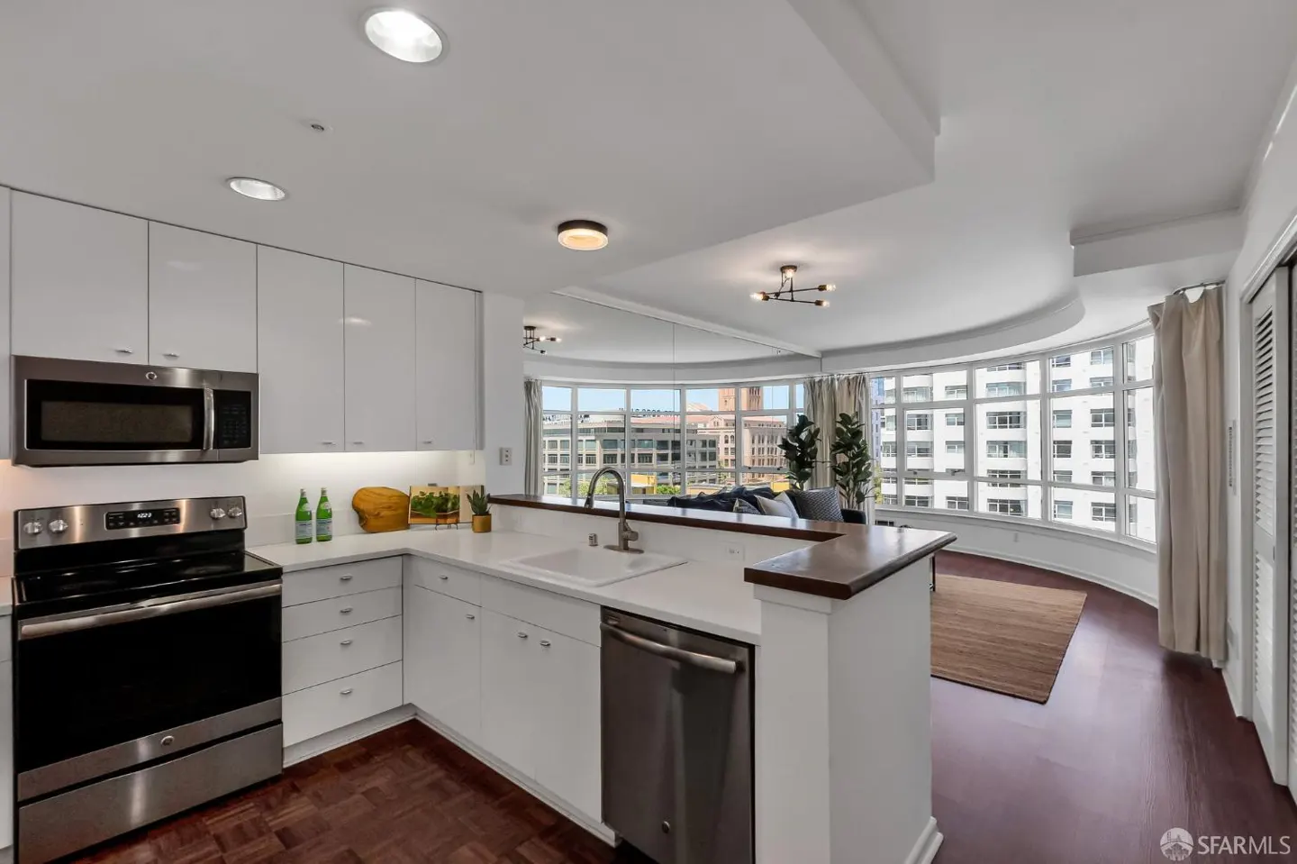 A modern kitchen with white cabinets, stainless steel appliances, and a large curved window overlooking a city.