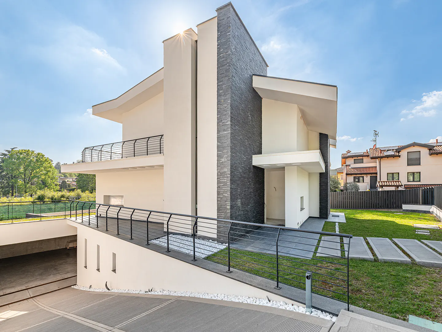 Modern two-story house with white walls, black stone accent, and black railings. A ramp leads to an underground garage.