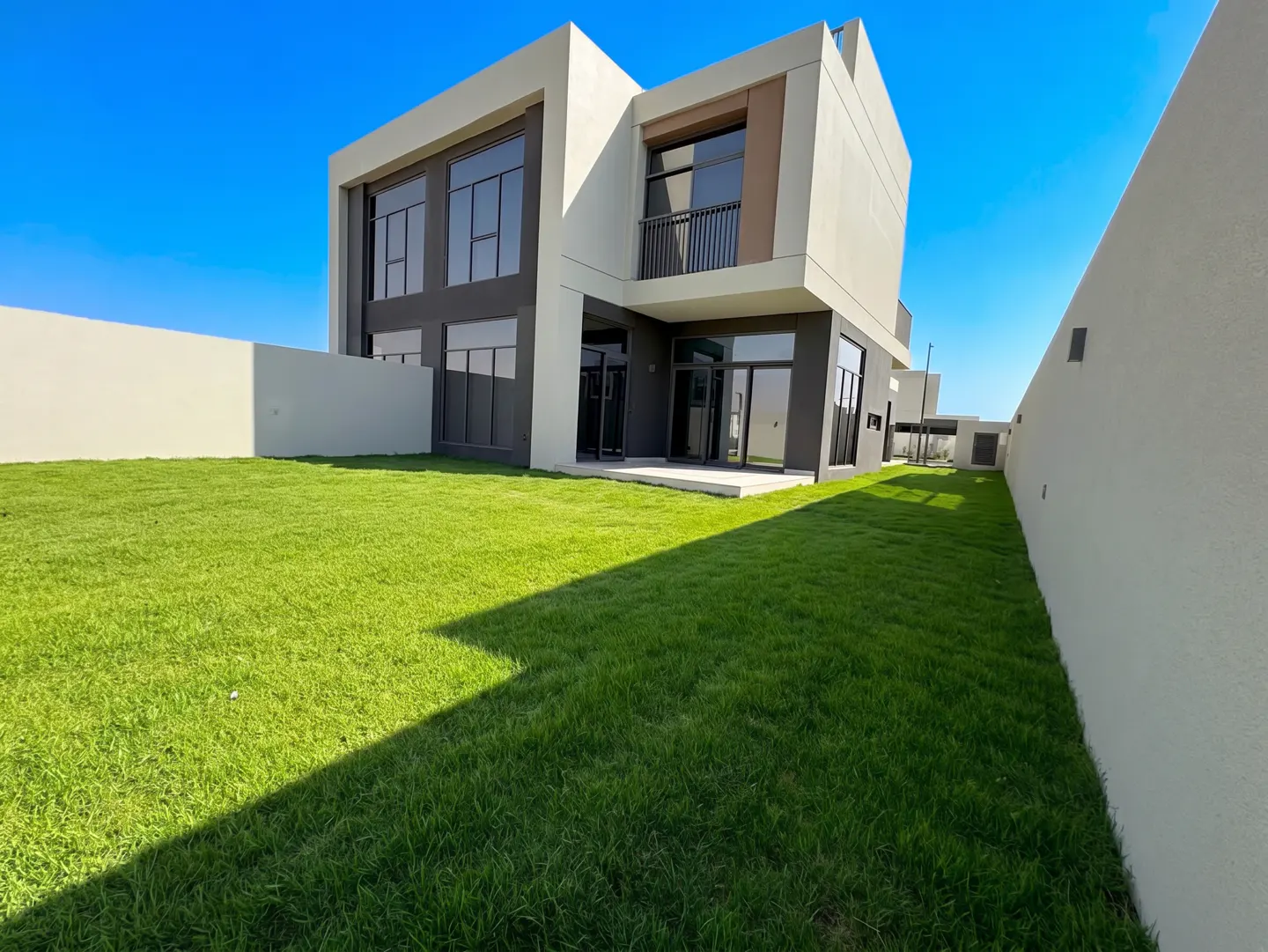 Two-story modern house with a green lawn and a white wall under a blue sky.
