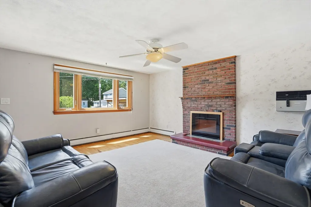 Living room with a brick fireplace, two black leather sofas, a window, and a ceiling fan.