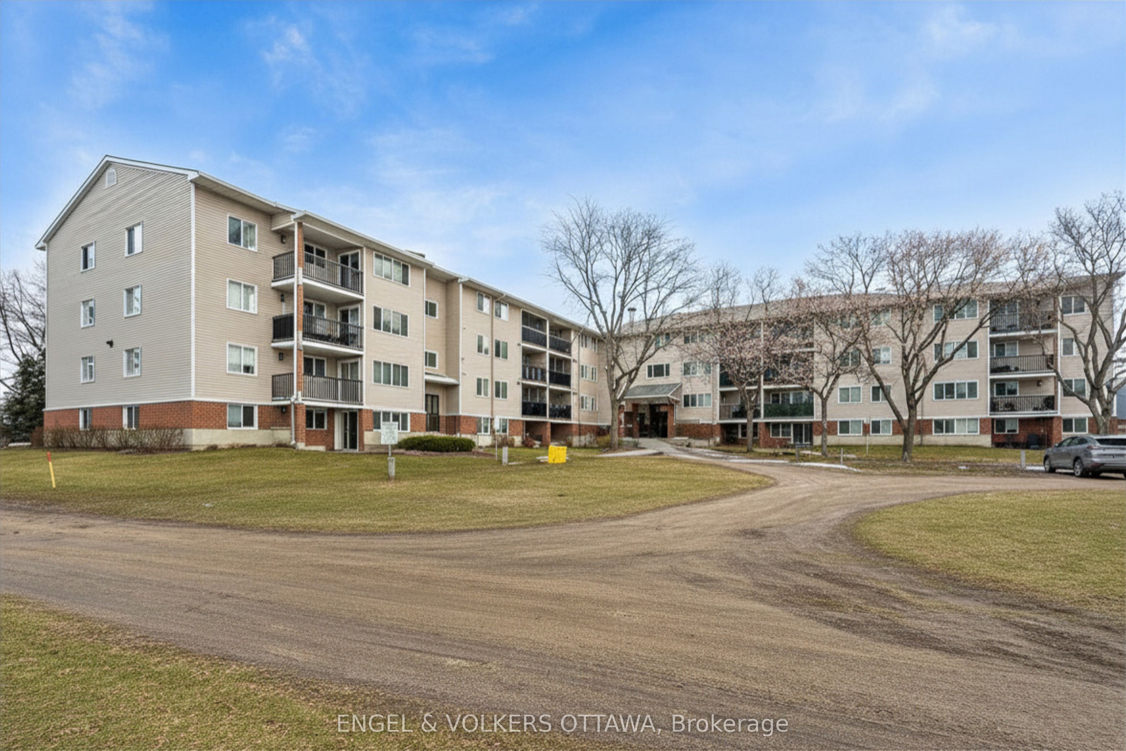 Exterior view of a beige apartment building with black balconies, a brick foundation, and a green lawn.