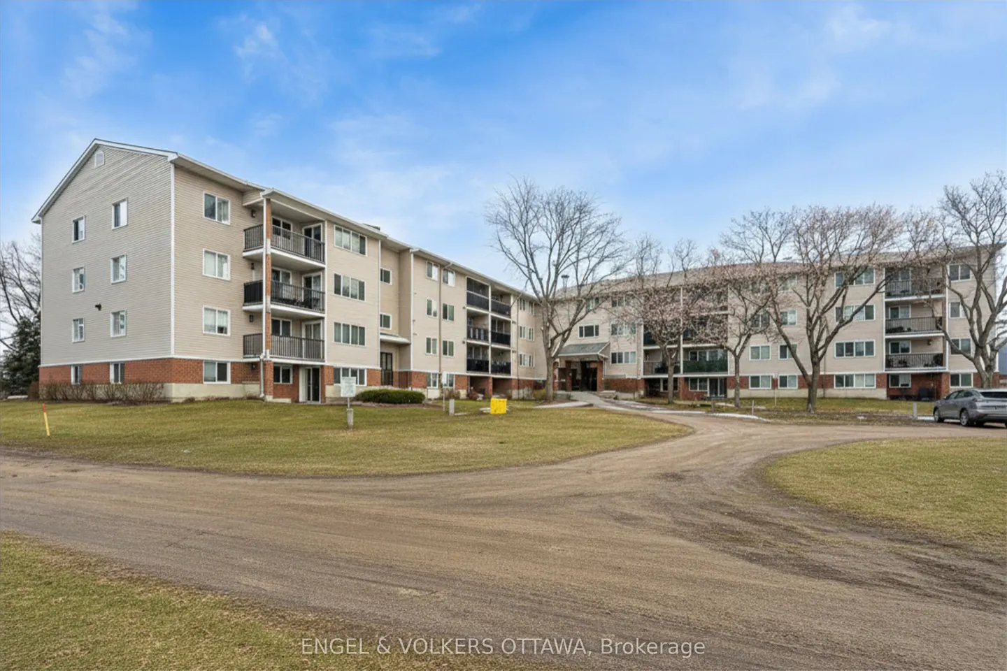 Exterior view of a beige apartment building with black balconies, a brick foundation, and a green lawn.