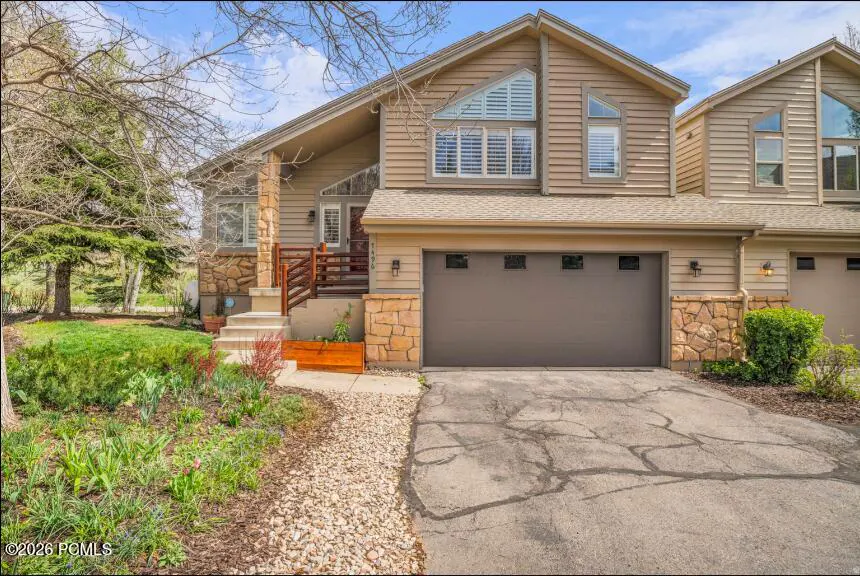 Tan two-story home with a brown garage door, stone accents, and a small front yard with flowers.