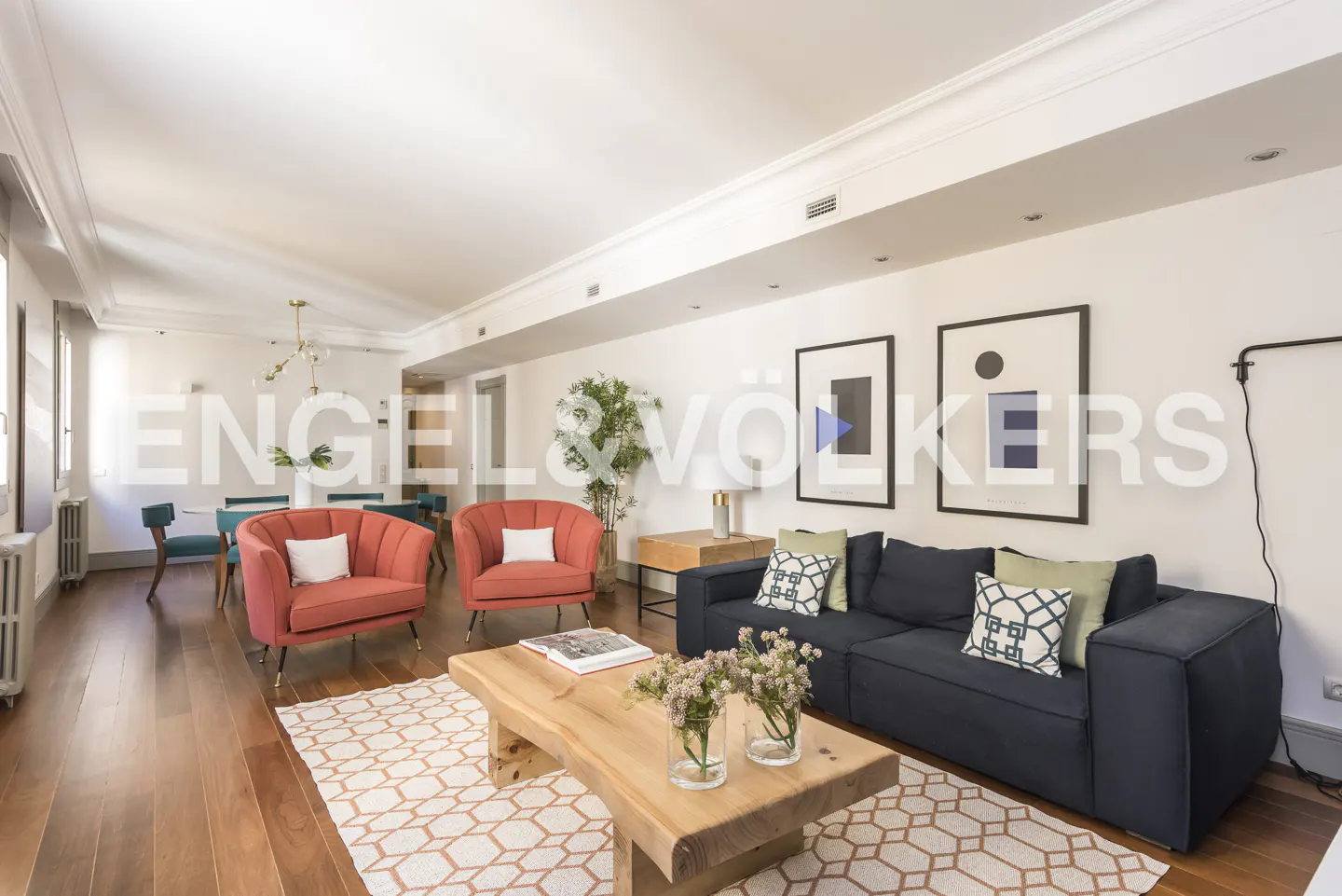 Bright living room with wood floors, coral chairs, a blue sofa, and a light wood coffee table with flowers.