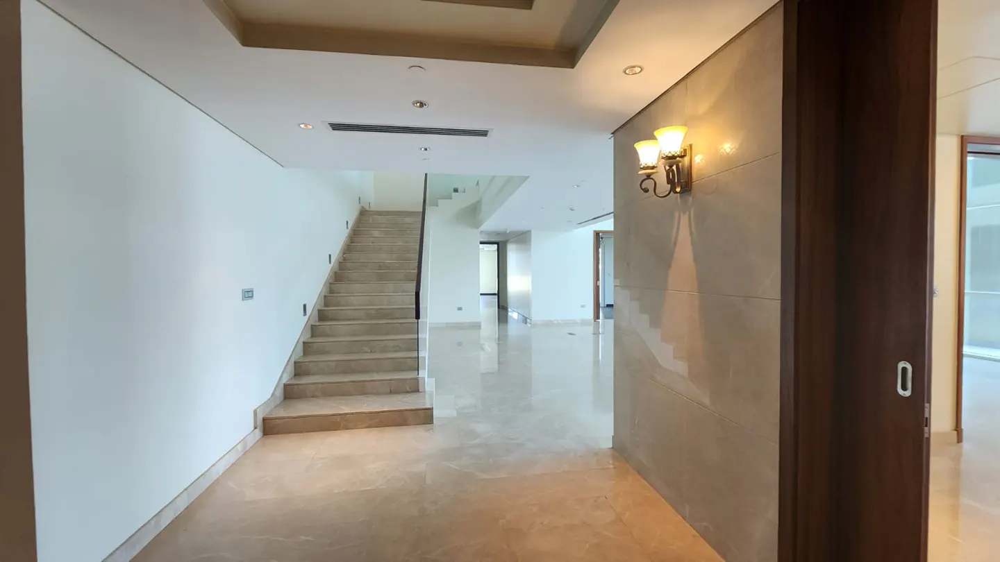 A bright foyer with marble floors, a staircase, and a decorative wall sconce.