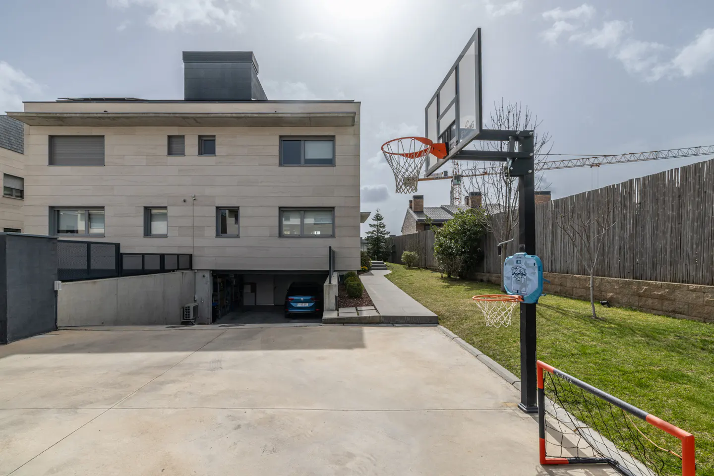 Modern house exterior with a driveway, basketball hoop, small soccer goal, and a blue car parked in the garage.