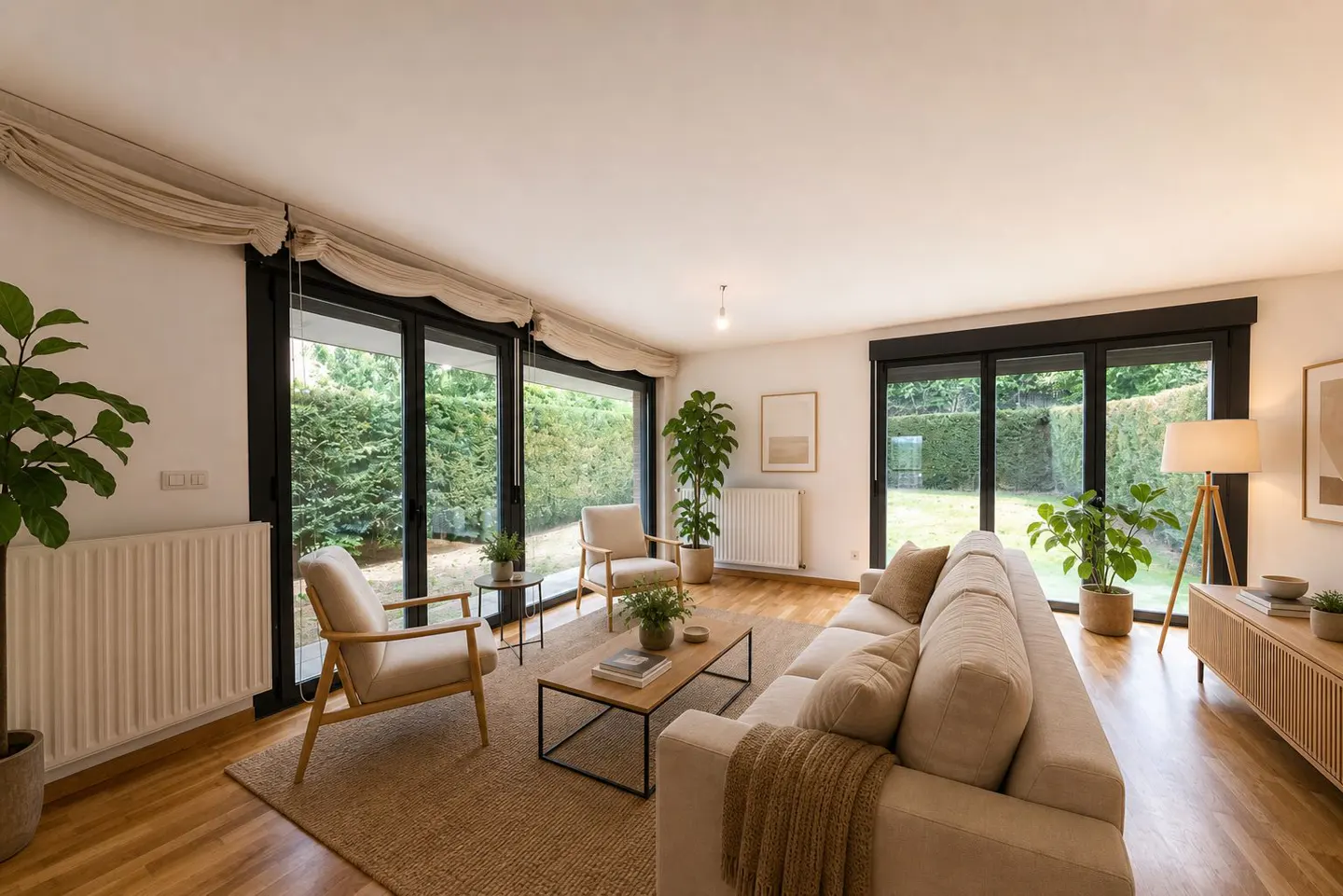 Bright living room with a beige sofa, two chairs, a wooden floor, and large windows overlooking a green garden.