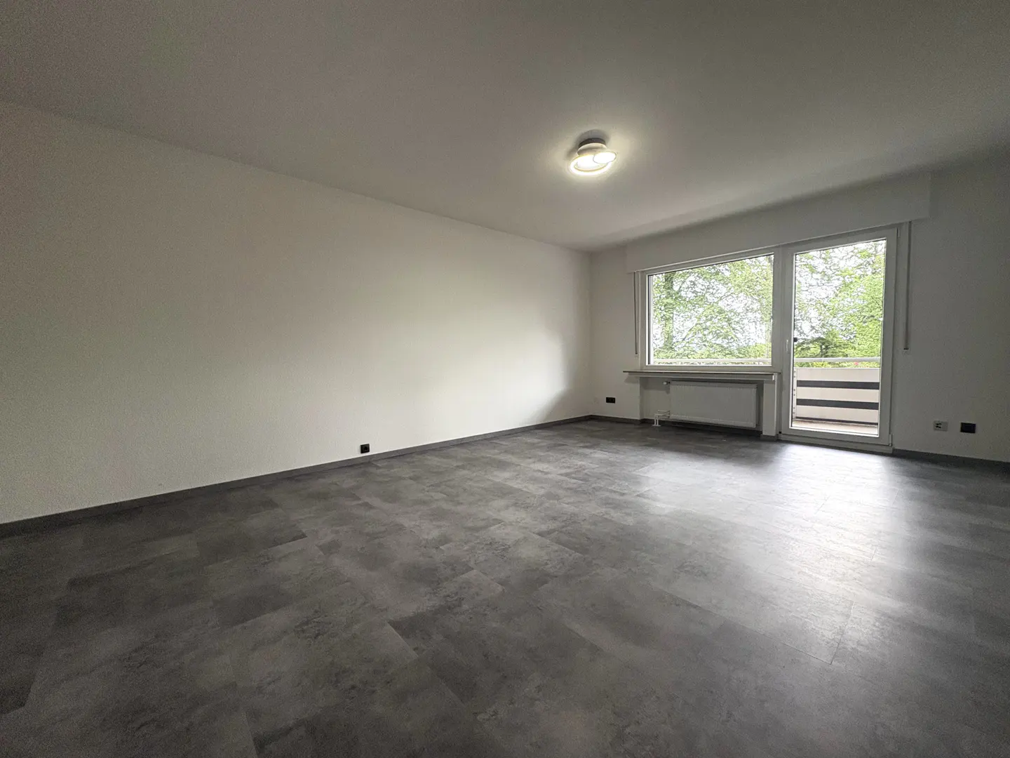 Empty room with white walls, grey stone-look flooring, a ceiling light, and a glass door leading to a balcony.