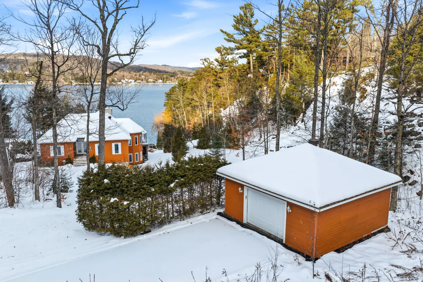 Winter view of an orange house and garage covered in snow, near a lake and trees.