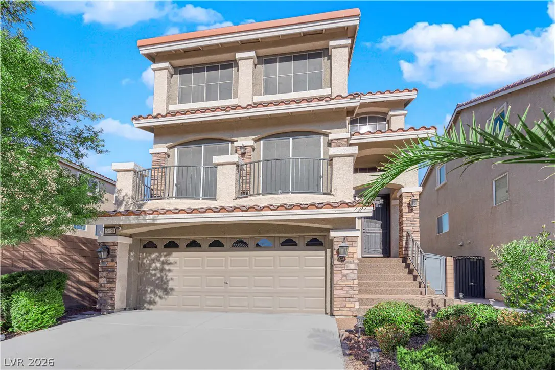 Two-story beige house with a brown garage door, a balcony, and a red tile roof.