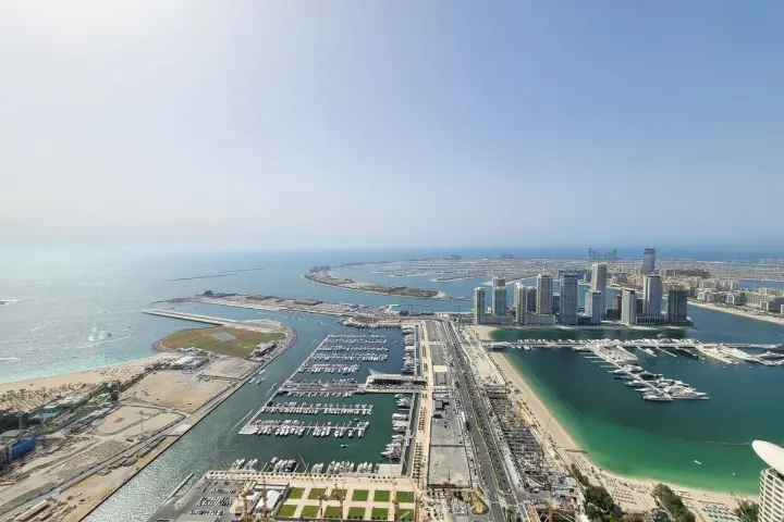 Aerial view of Dubai's skyline, featuring modern high-rise buildings, a marina filled with yachts, and the Palm Jumeirah island.