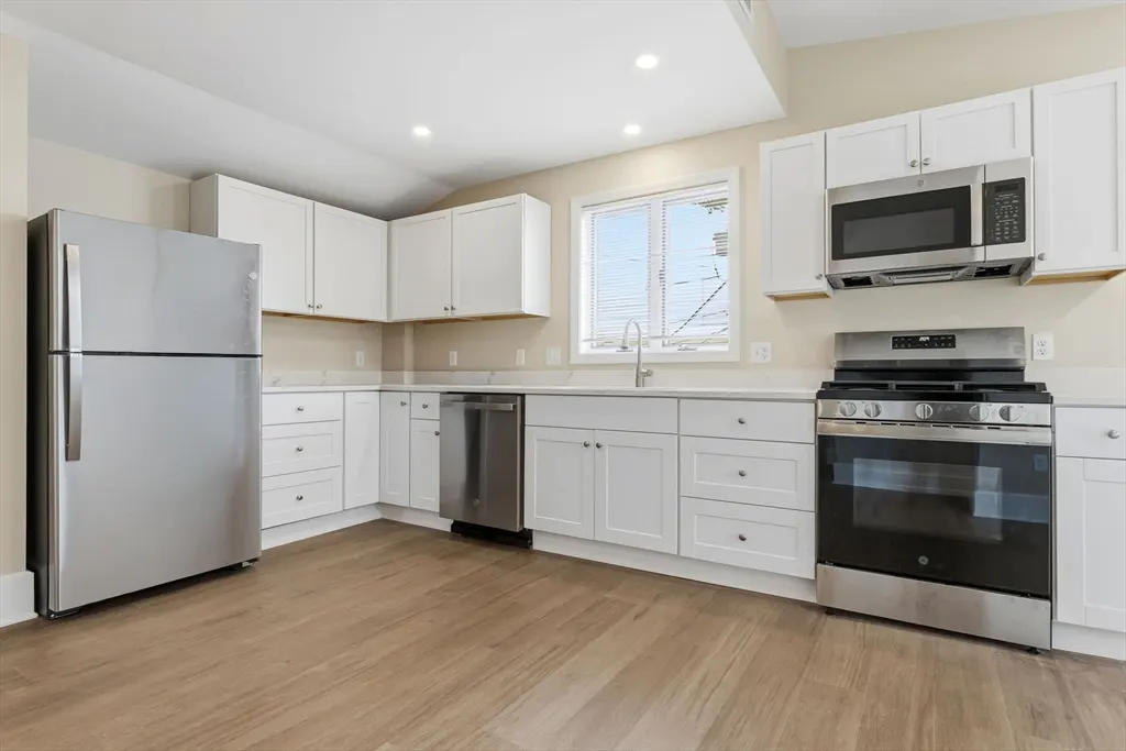 Bright kitchen with stainless steel appliances, white cabinets, light wood floors, and a window.