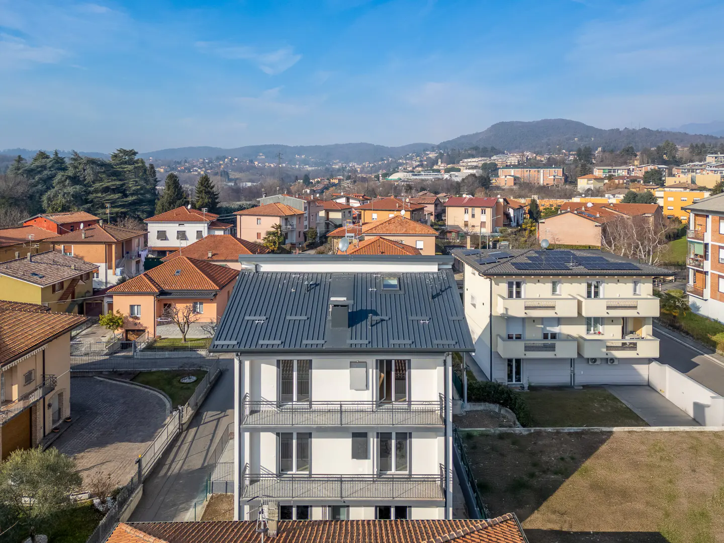 Aerial view of a three-story white building with balconies and a gray metal roof in a residential neighborhood.