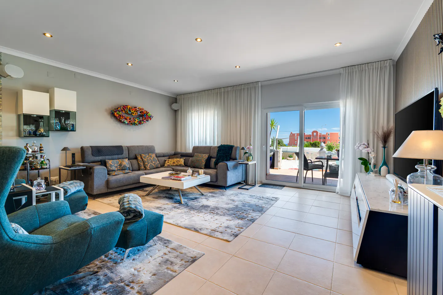 Bright living room with gray sectional sofa, blue armchairs, white coffee table, and sliding glass doors to a patio.
