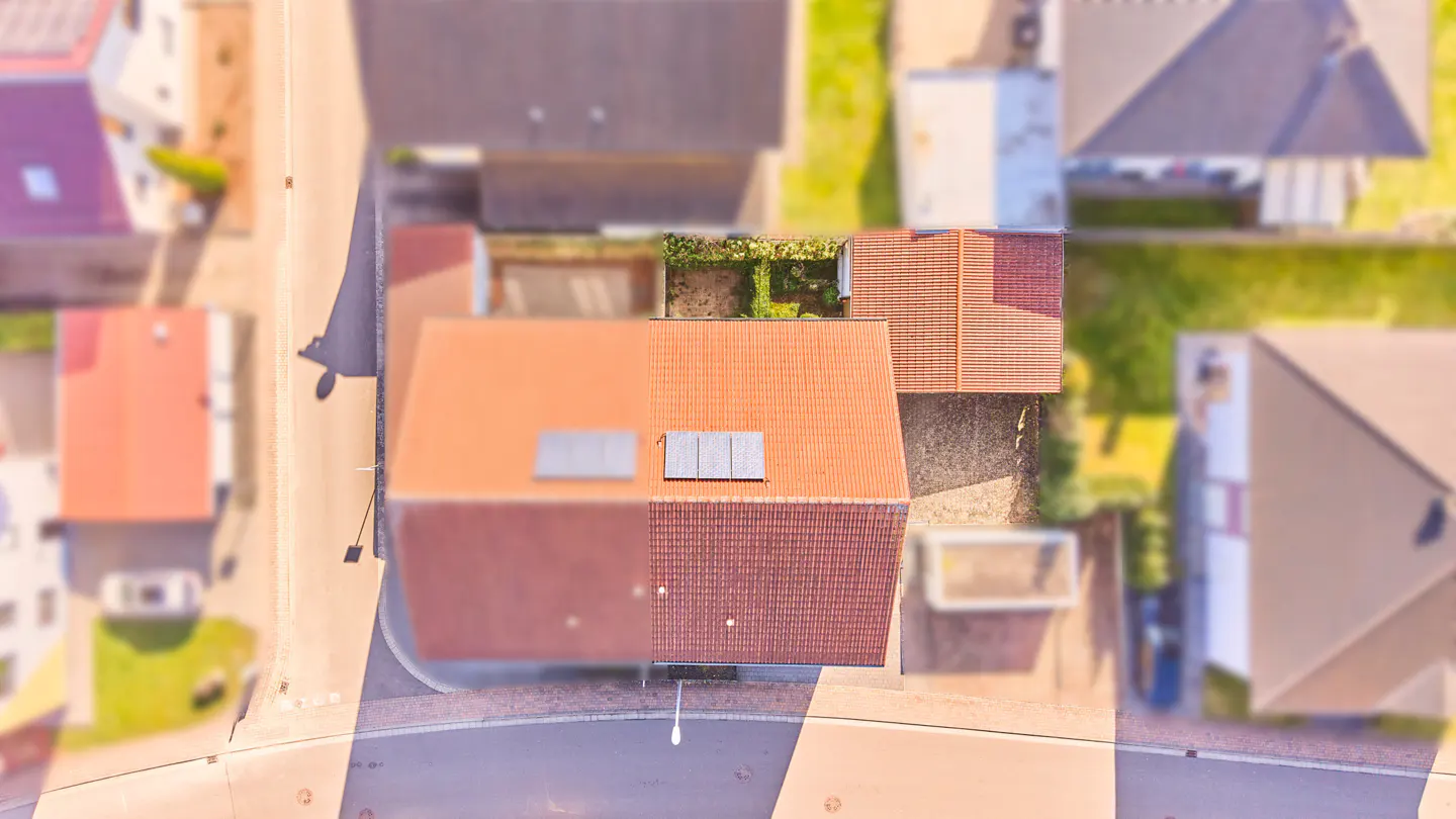 Aerial view of a house with a terracotta tiled roof and solar panels, surrounded by a neighborhood with paved streets.