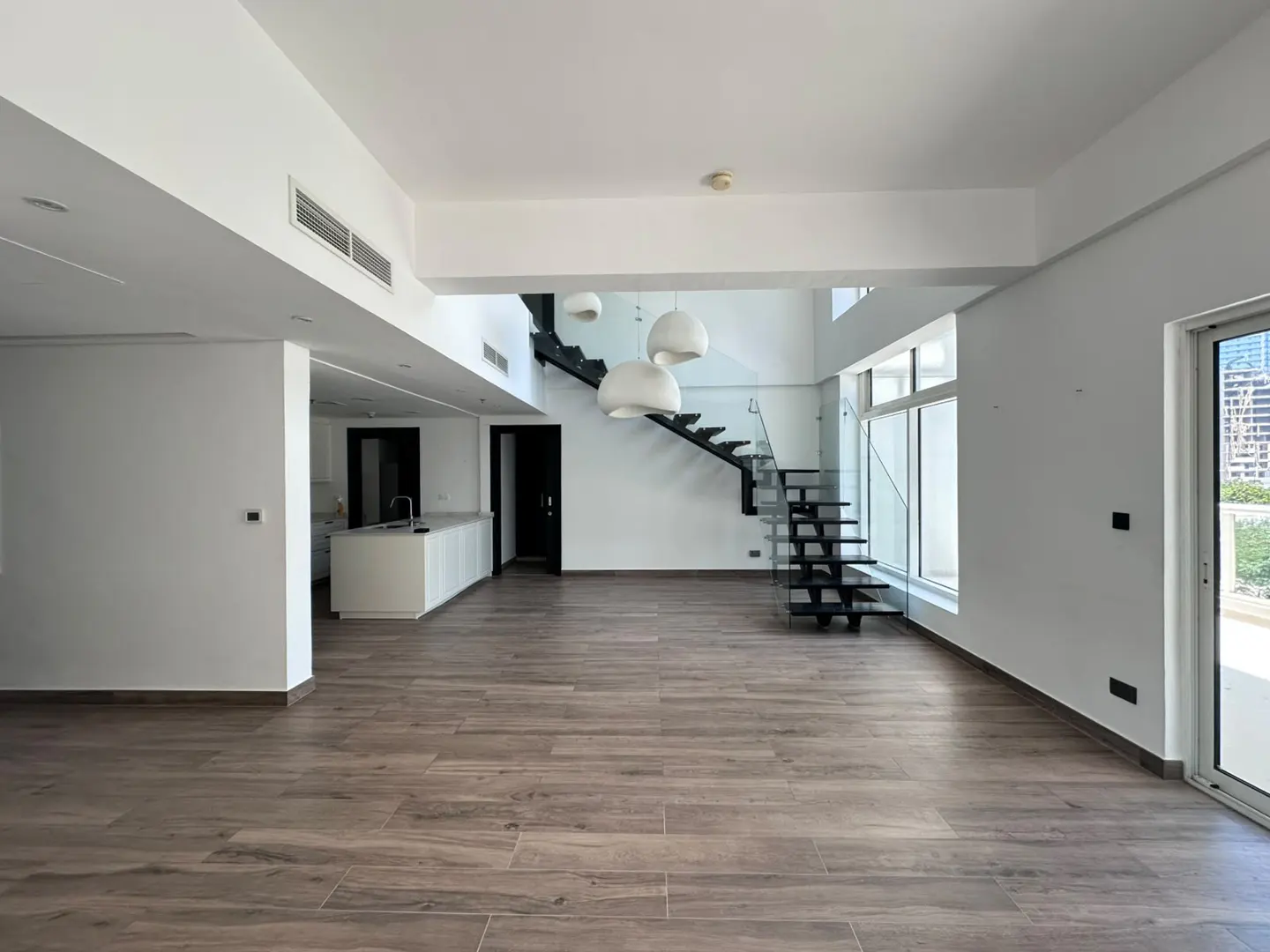 Modern open-plan living area with wood-look tile floors, a white kitchen island, and a floating staircase with glass railing.