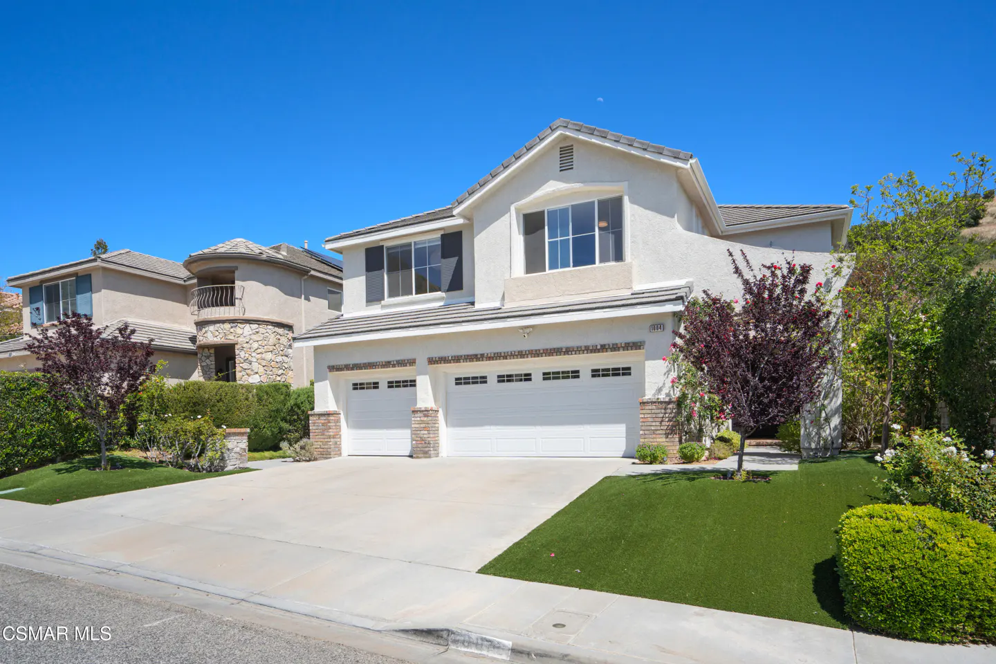 Two-story stucco house with a two-car garage, green lawn, and blue sky.