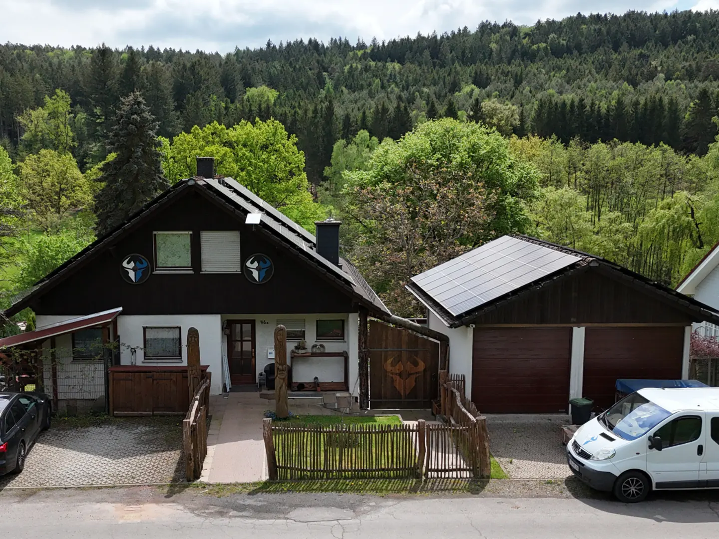 A two-story house with solar panels on the roof, a garage, and a forest in the background.