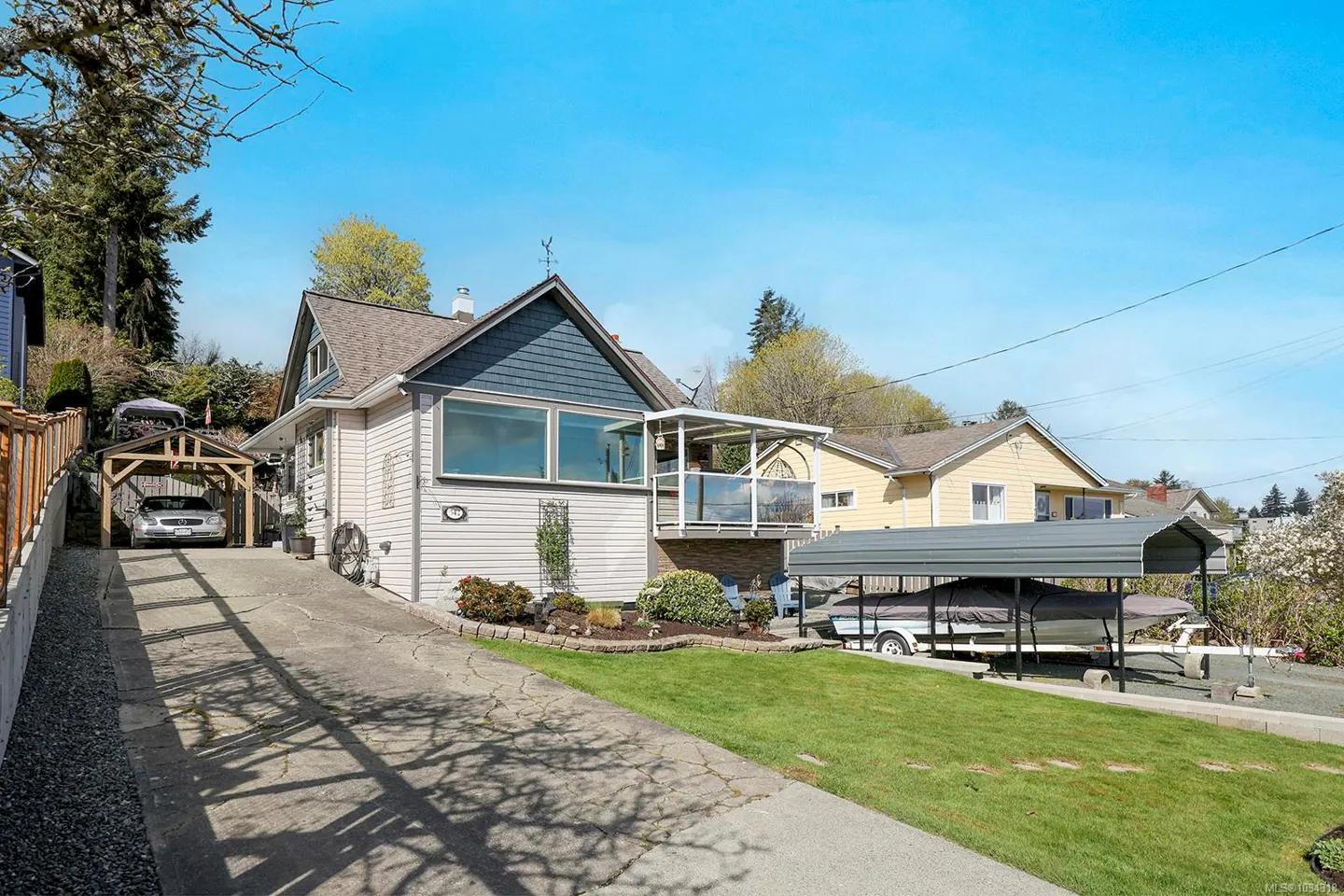 Exterior of a two-story house with a blue roof, a car port, and a boat port on a sunny day.