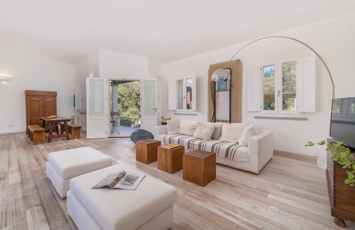 Bright living room with white walls, wood floors, and white furniture. Open doors lead to a patio. A vintage gas pump adds a unique touch.
