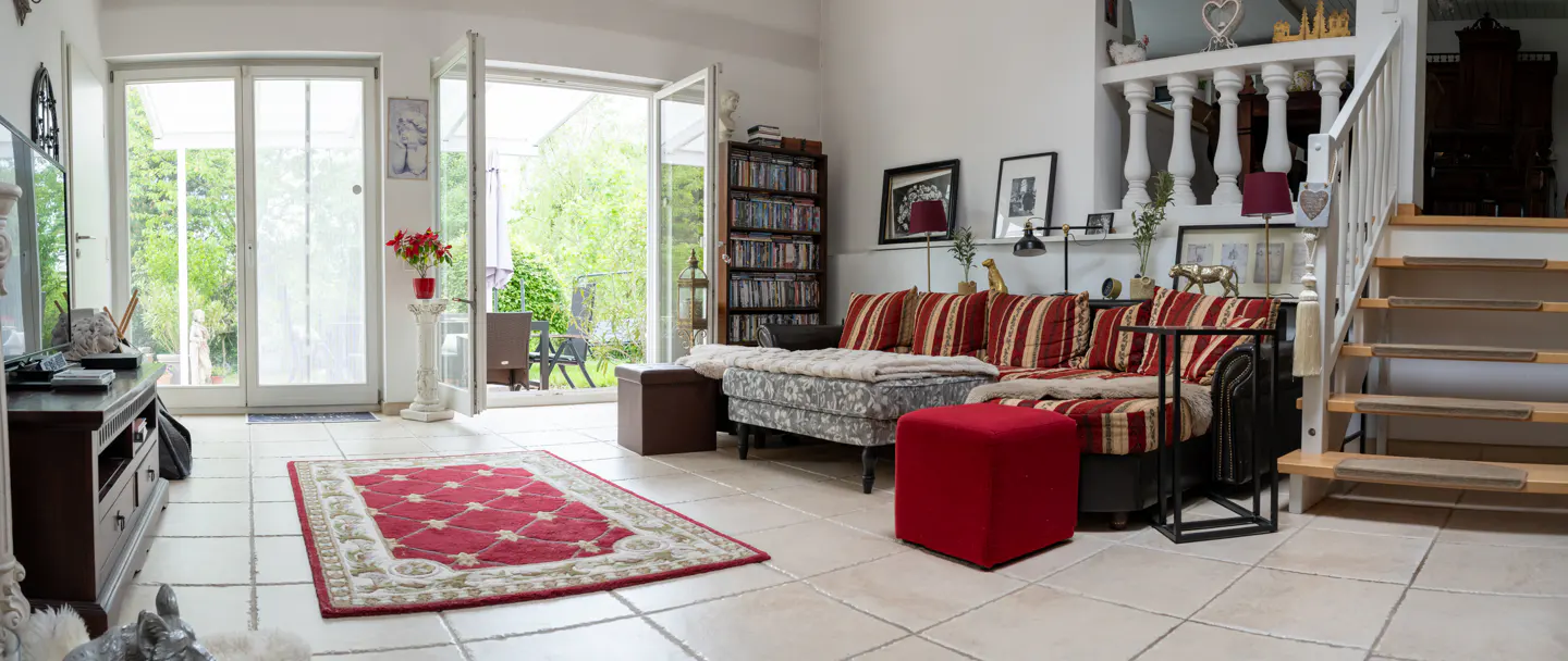 Bright living room with open patio doors. Red striped sofa, red rug, and staircase with white banister.
