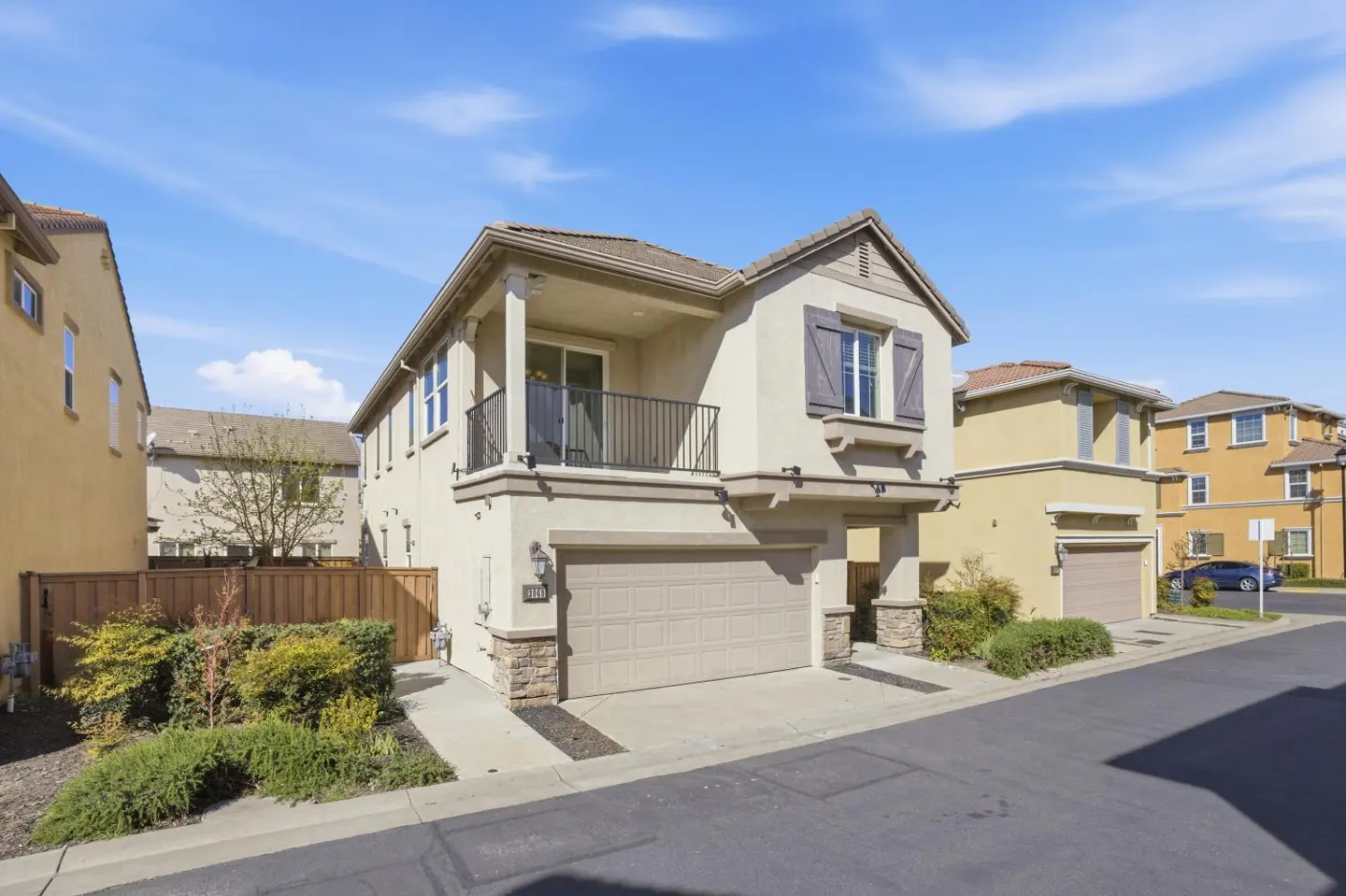 Beige two-story house with a balcony, a garage, and gray shutters under a blue sky.