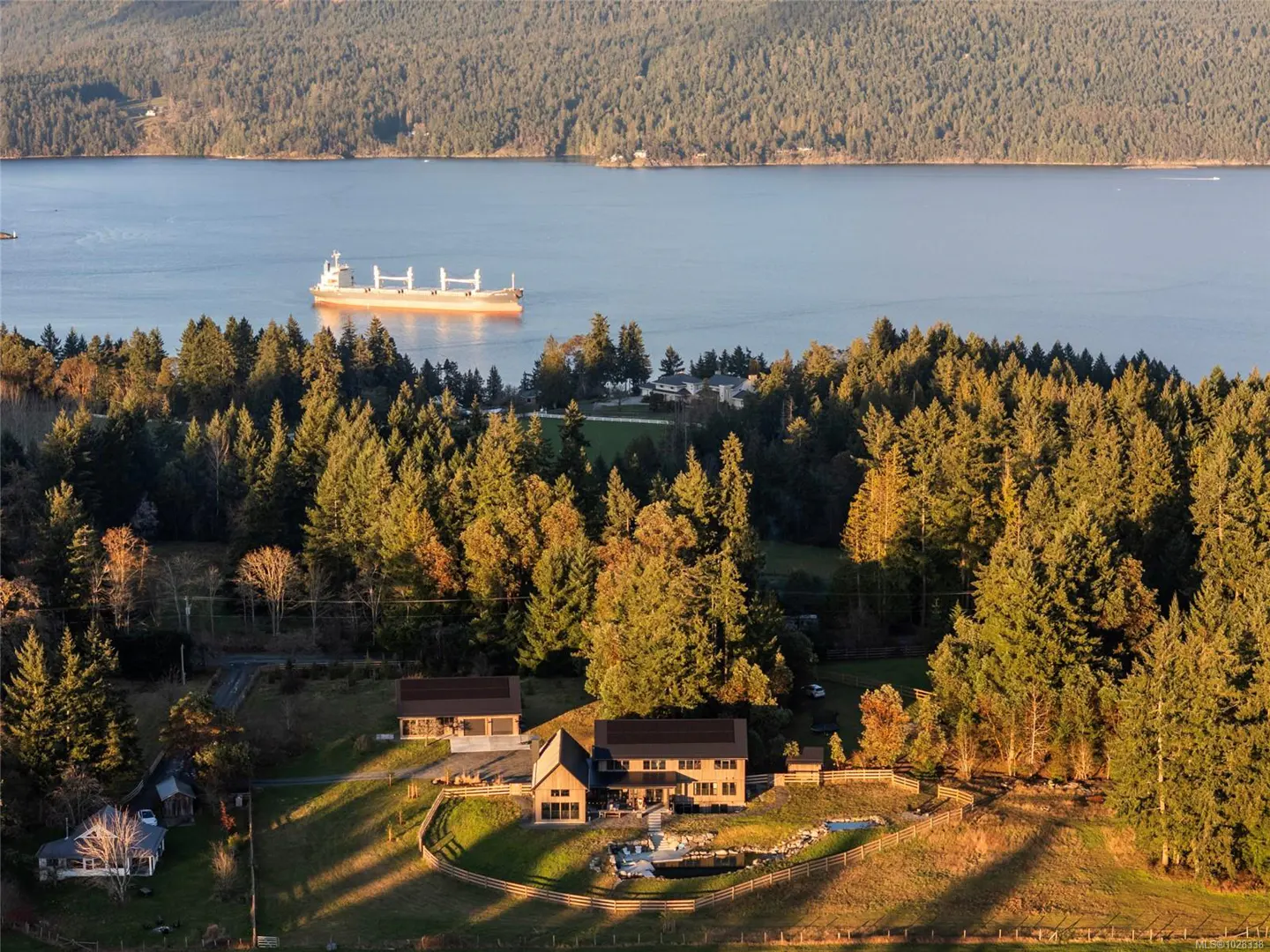 Aerial view of a modern home nestled in trees, overlooking a bay with a cargo ship.