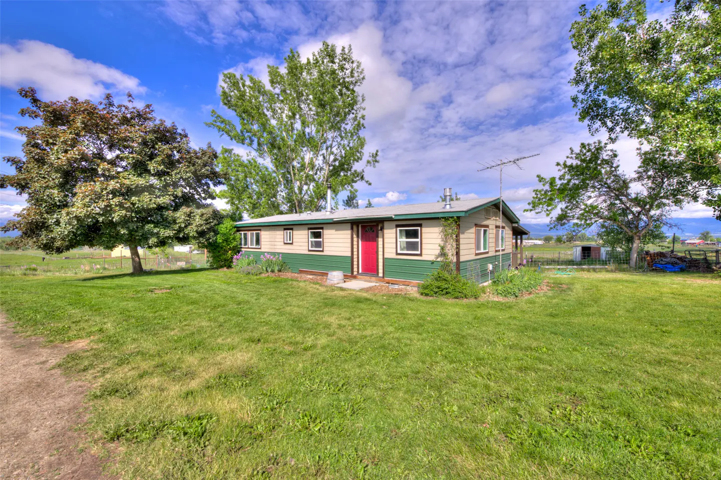 Single-story home with tan and green siding, a bright red front door, and a large grassy yard under a blue sky.