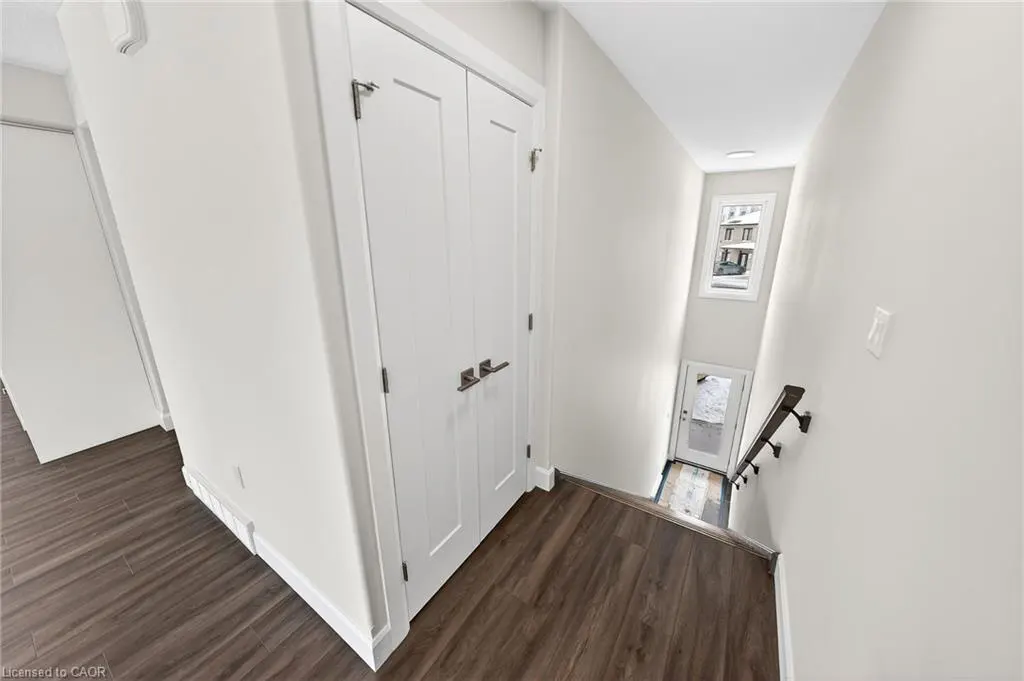 Hallway with dark wood floors, white walls, and a white closet. Stairs lead down to a door with a window above.