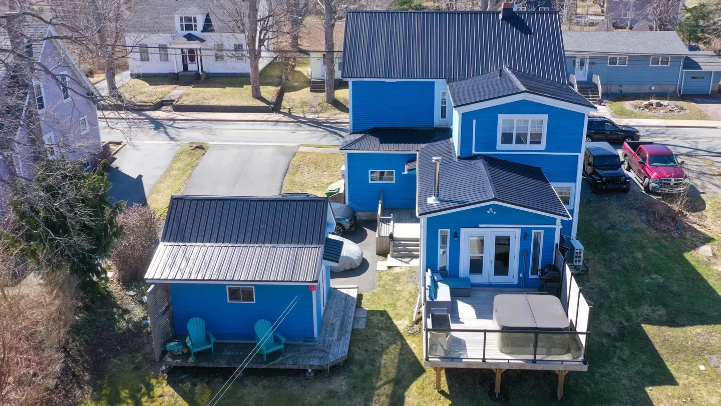 Aerial view of a blue house with a black roof, a hot tub on the deck, and teal Adirondack chairs.