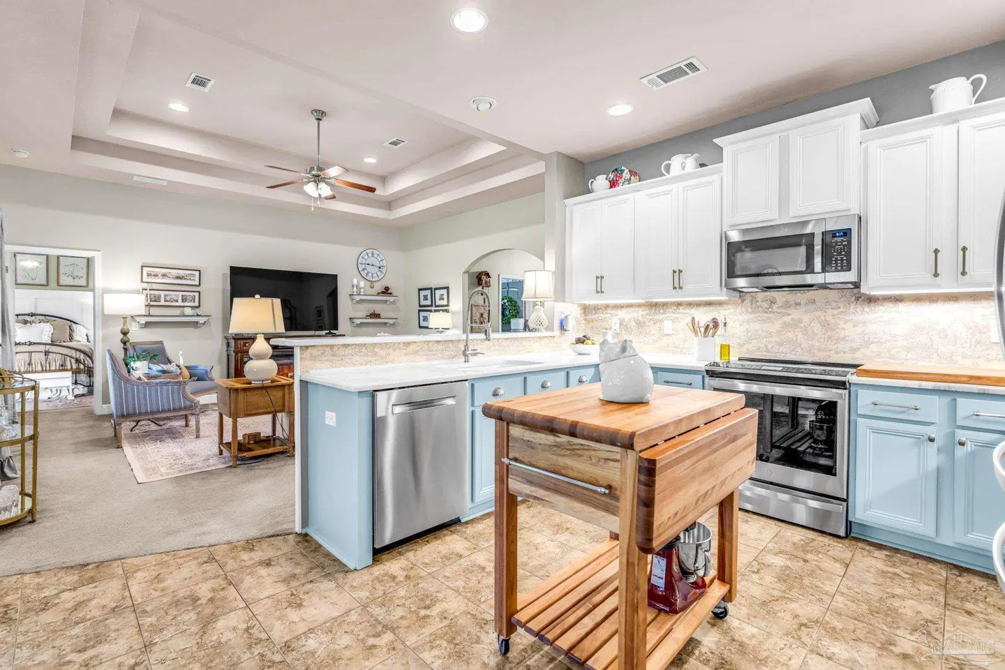 Open concept kitchen with light blue cabinets, white countertops, stainless steel appliances, and a wooden kitchen island. Living room in background.