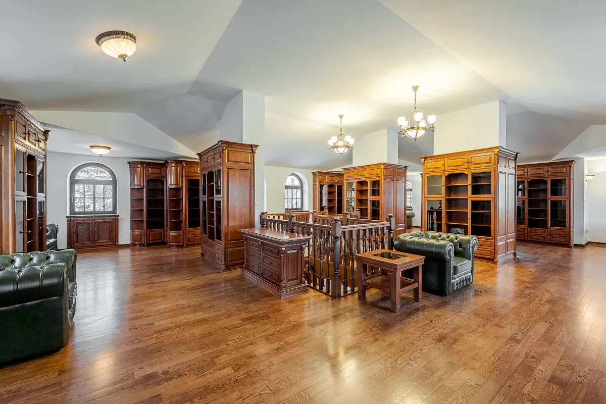 A spacious library with hardwood floors, filled with dark wood bookcases, a green leather sofa, and a staircase.