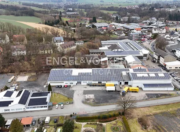Aerial view of a commercial building with solar panels on the roof, surrounded by trees and other buildings.
