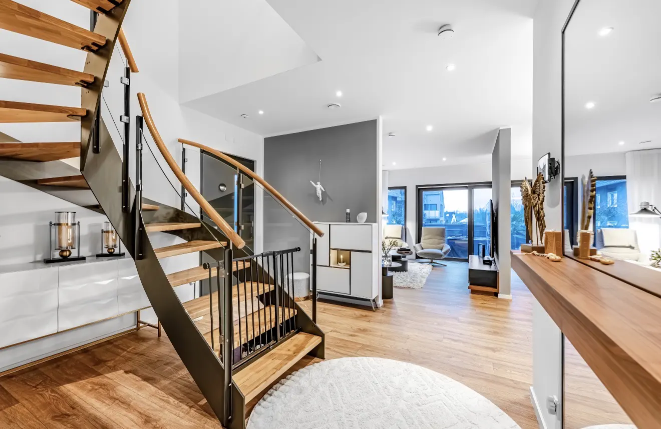 Bright, modern home interior with wood floors, a staircase with wood steps and metal railings, and an open living area with white furniture.