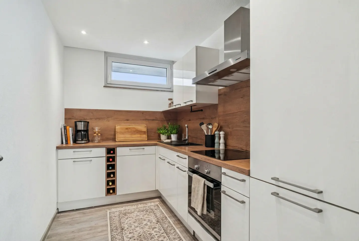 A modern kitchen with white cabinets, wood countertops, and stainless steel appliances. A patterned rug lies on the floor.
