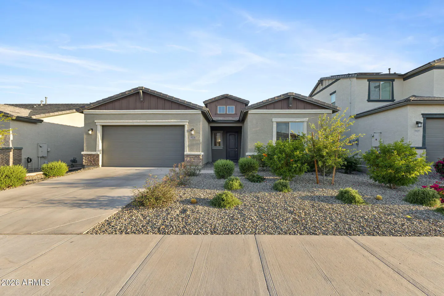 A single-story house with a gray garage door, brown roof, and rock landscaping.