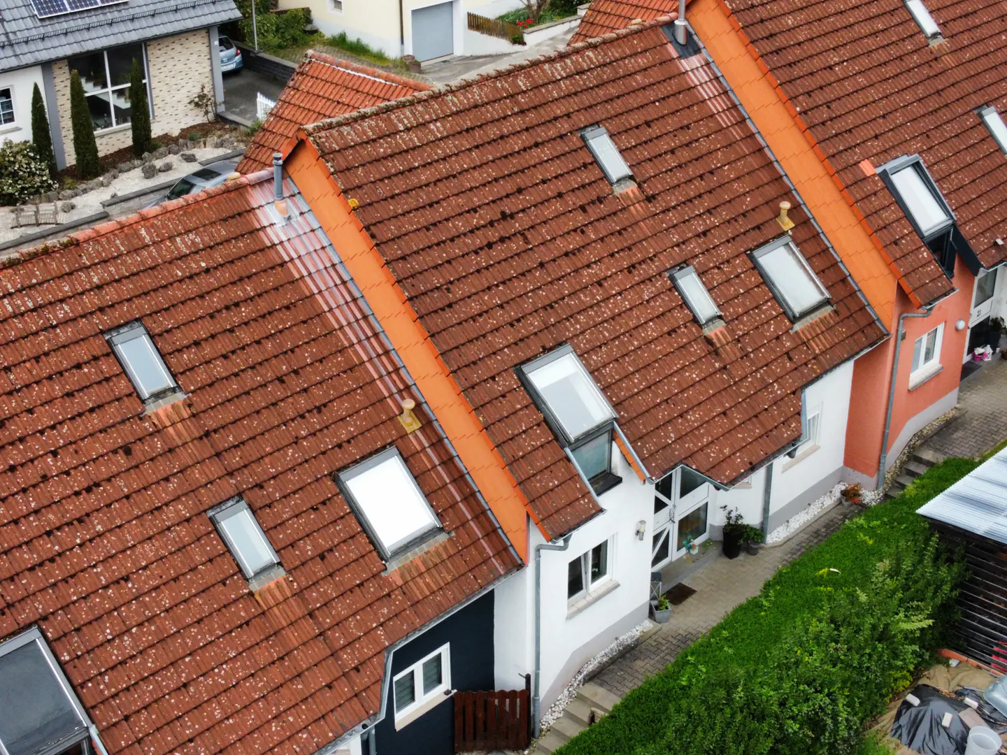 Aerial view of row houses with red tile roofs and skylights, separated by orange dividers and green hedges.