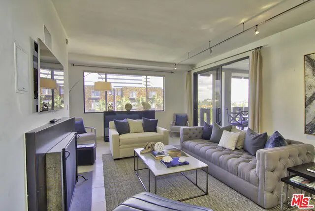 Living room with a gray sofa, a cream loveseat, and a marble coffee table on a gray rug. A sliding glass door leads to a balcony.