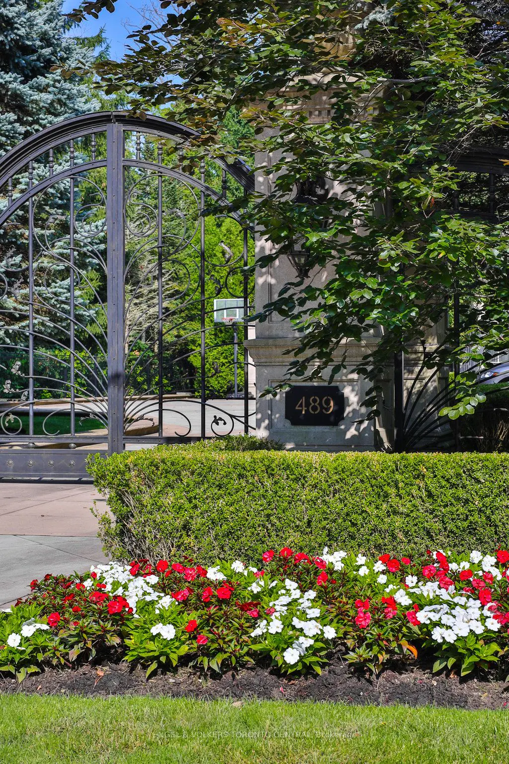 Gated entrance to a property with red and white flowers in front of a trimmed green hedge. The house number 489 is visible.