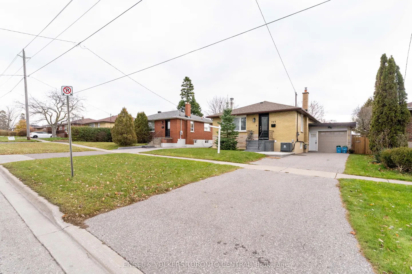 Street view of two single-story houses with driveways and lawns on a cloudy day. One house is yellow brick, the other is red brick.