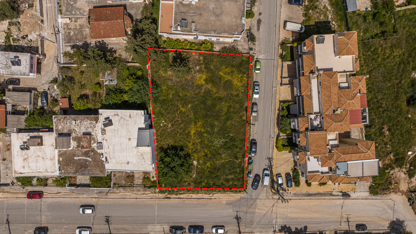 Aerial view of a vacant lot outlined in red, surrounded by houses and a street with parked cars.